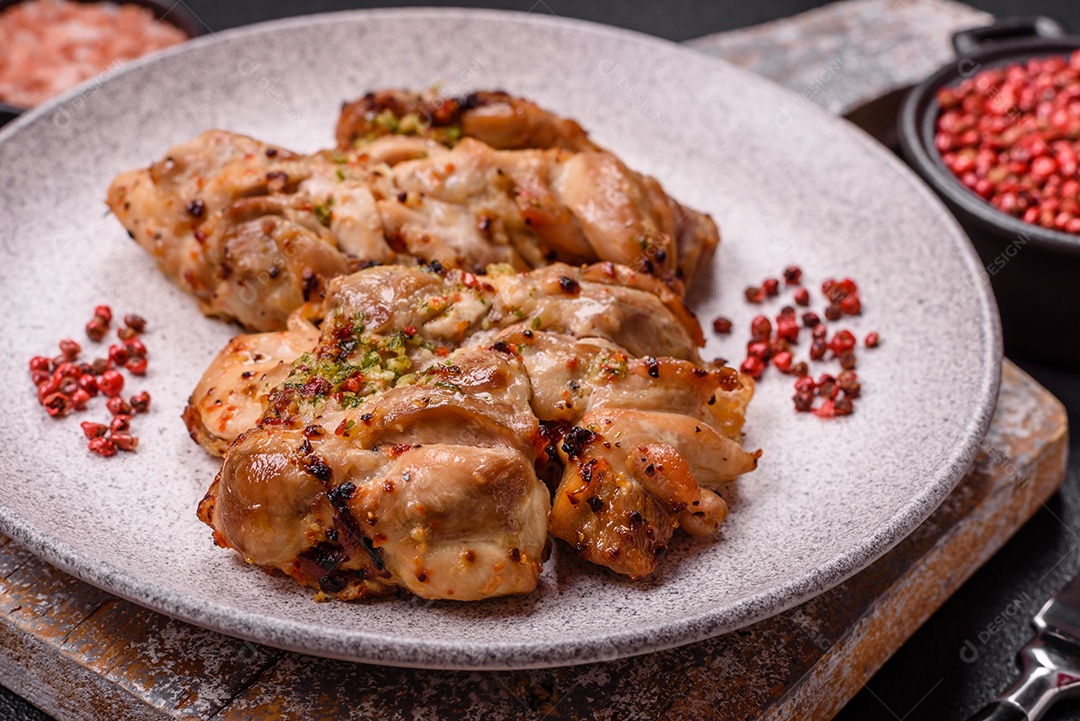 A imagem mostra sobrecoxas de frango grelhadas, servidas em um prato escuro com temperos
