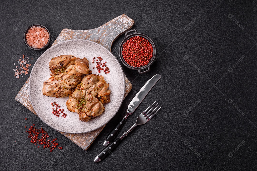 A imagem mostra sobrecoxas de frango grelhadas, servidas em um prato escuro com temperos