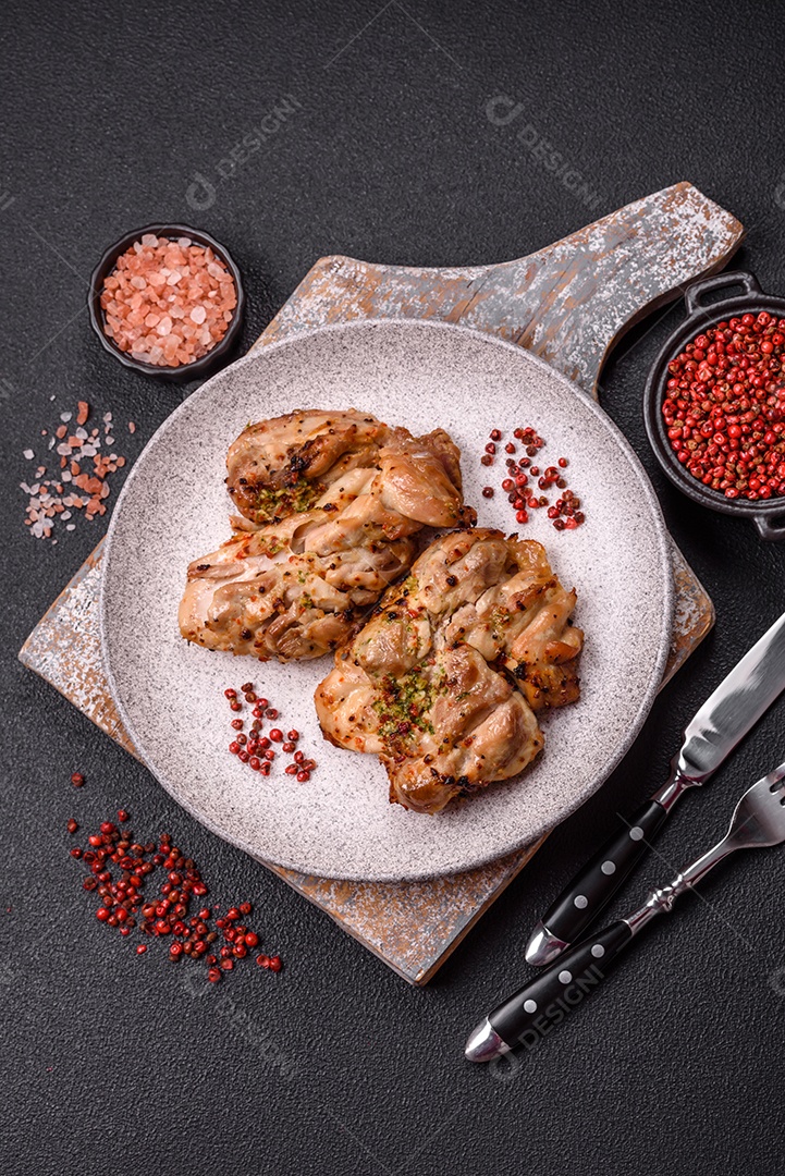 A imagem mostra sobrecoxas de frango grelhadas, servidas em um prato escuro com temperos