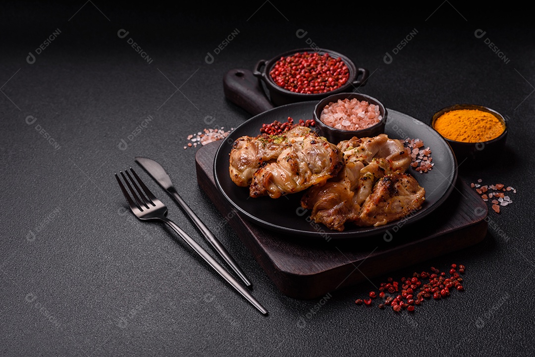 A imagem mostra sobrecoxas de frango grelhadas, servidas em um prato escuro com temperos