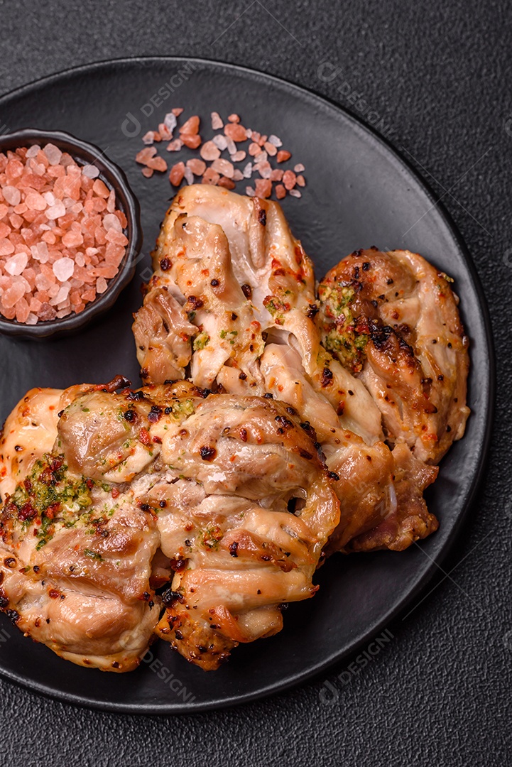 A imagem mostra sobrecoxas de frango grelhadas, servidas em um prato escuro com temperos