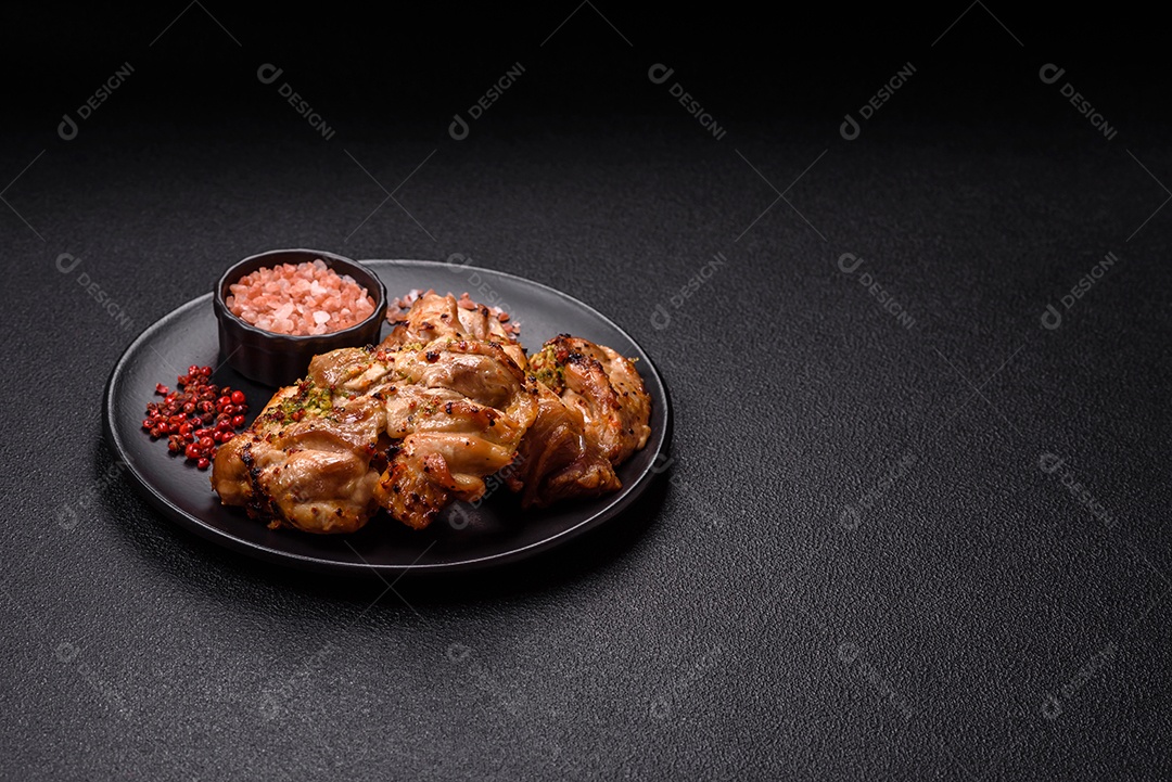 A imagem mostra sobrecoxas de frango grelhadas, servidas em um prato escuro com temperos