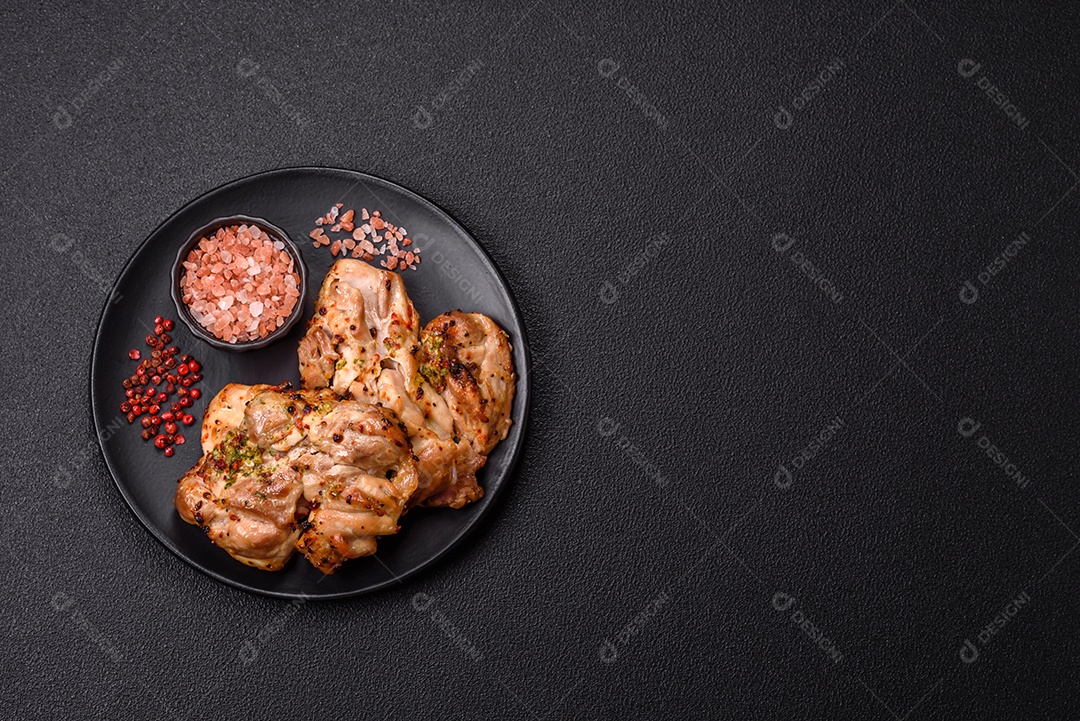 A imagem mostra sobrecoxas de frango grelhadas, servidas em um prato escuro com temperos