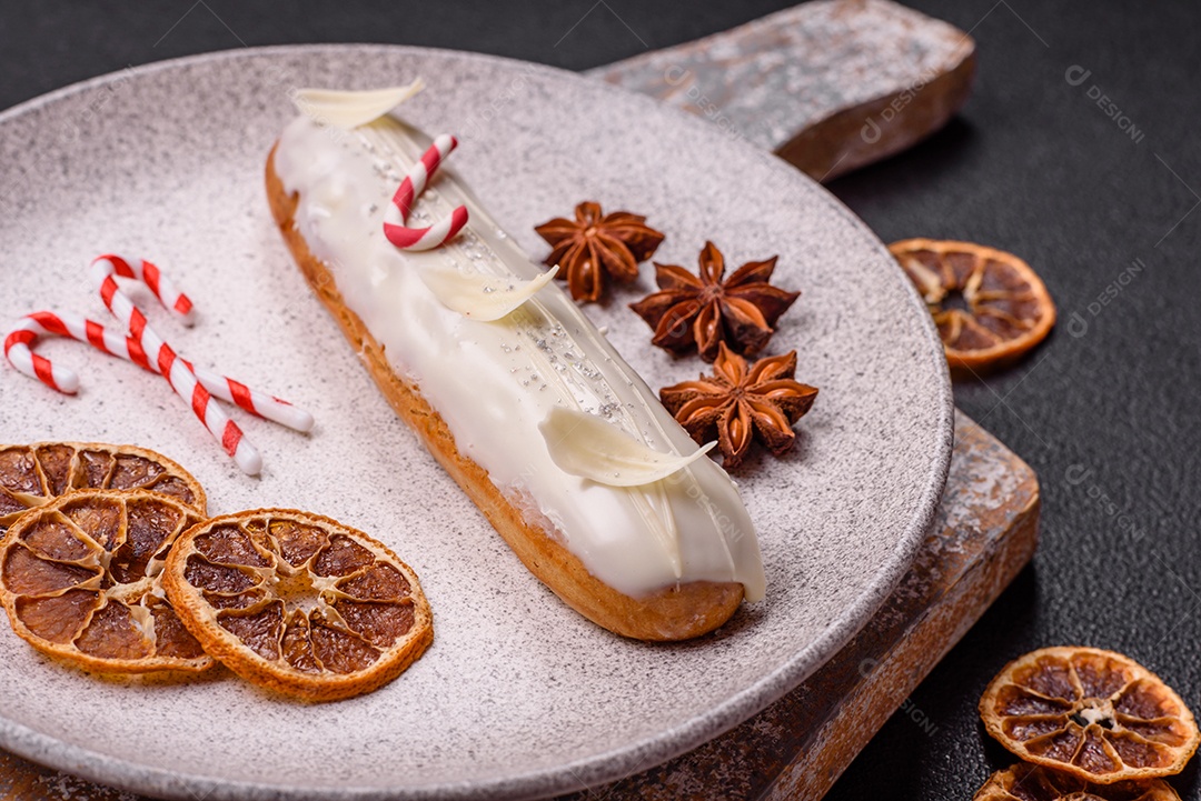 A imagem mostra uma bomba de chocolate, também conhecida como éclair, servida com rodelas de laranja desidratada e anis estrelado