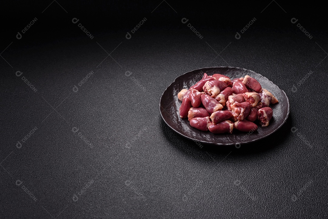 A imagem mostra corações de frango crus em uma tábua de madeira, acompanhados de pimenta rosa e tomates-cereja.,
