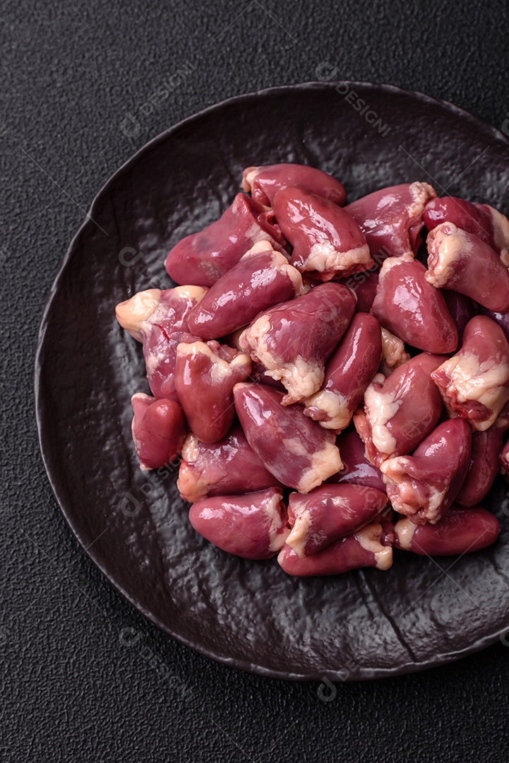 A imagem mostra corações de frango crus em uma tábua de madeira, acompanhados de pimenta rosa e tomates-cereja.