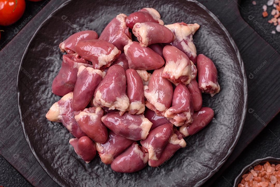 A imagem mostra corações de frango crus em uma tábua de madeira, acompanhados de pimenta rosa e tomates-cereja.