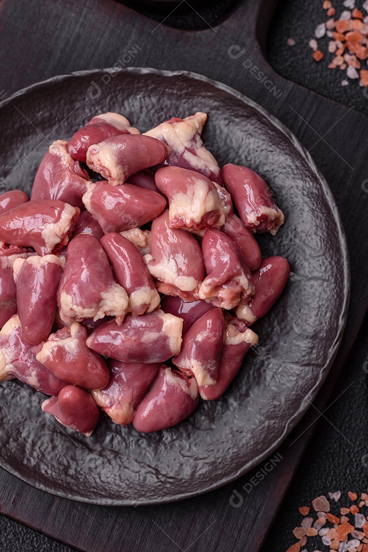 A imagem mostra corações de frango crus em uma tábua de madeira, acompanhados de pimenta rosa e tomates-cereja.