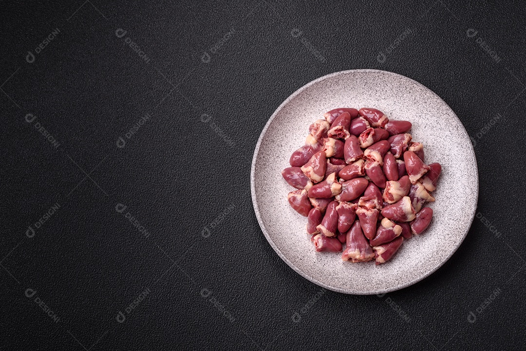 A imagem mostra corações de frango crus em uma tábua de madeira, acompanhados de pimenta rosa e tomates-cereja.