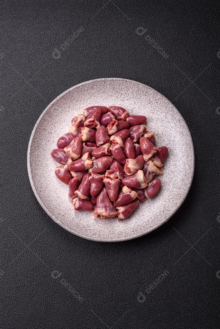 A imagem mostra corações de frango crus em uma tábua de madeira, acompanhados de pimenta rosa e tomates-cereja.