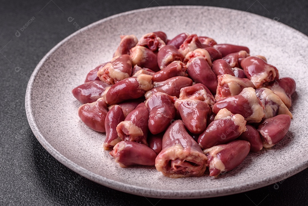 A imagem mostra corações de frango crus em uma tábua de madeira, acompanhados de pimenta rosa e tomates-cereja.