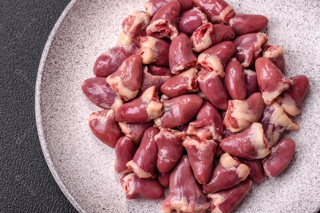 A imagem mostra corações de frango crus em uma tábua de madeira, acompanhados de pimenta rosa e tomates-cereja.
