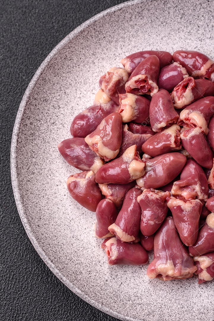 A imagem mostra corações de frango crus em uma tábua de madeira, acompanhados de pimenta rosa e tomates-cereja.