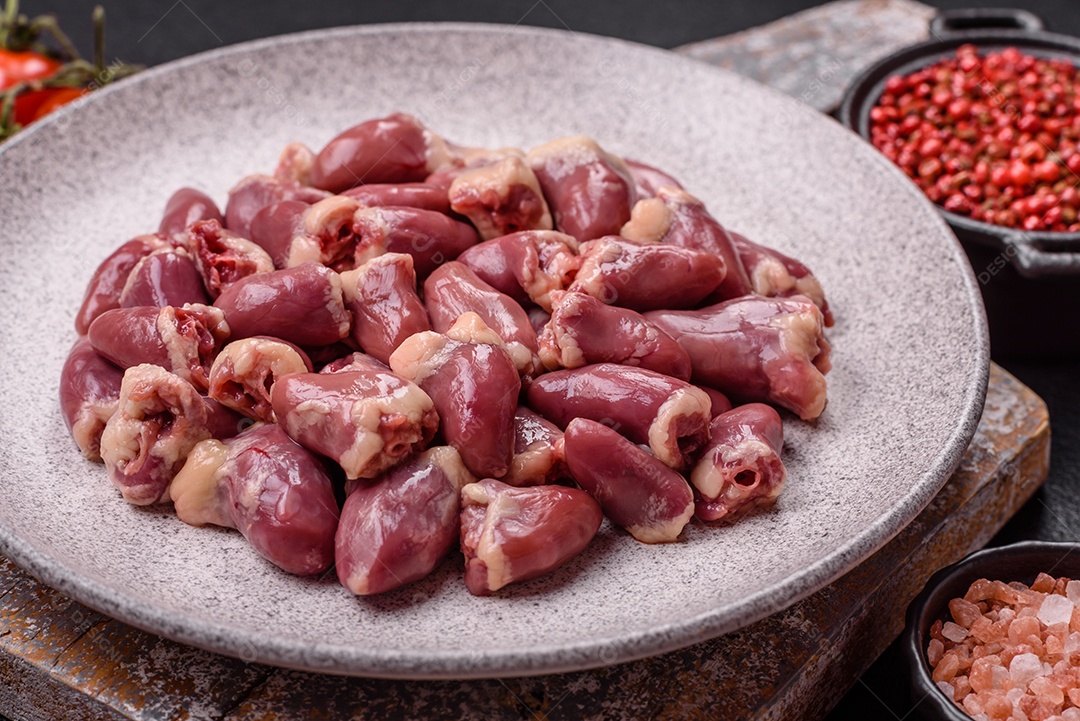 A imagem mostra corações de frango crus em uma tábua de madeira, acompanhados de pimenta rosa e tomates-cereja.
