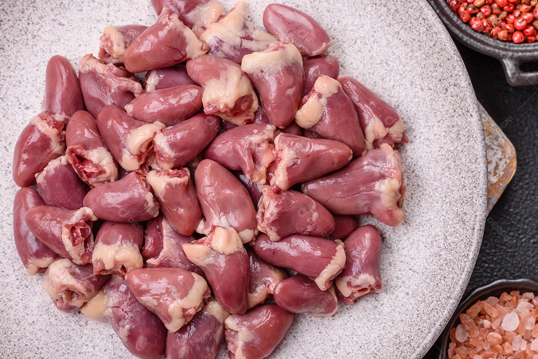 A imagem mostra corações de frango crus em uma tábua de madeira, acompanhados de pimenta rosa e tomates-cereja.