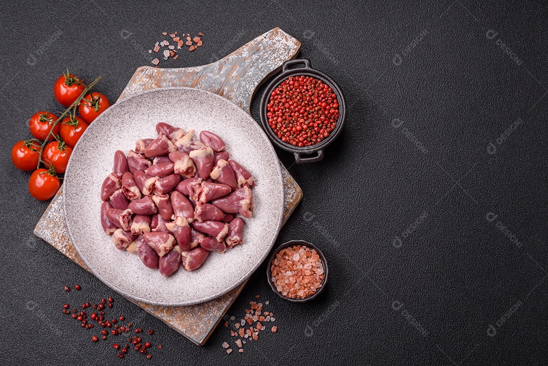 A imagem mostra corações de frango crus em uma tábua de madeira, acompanhados de pimenta rosa e tomates-cereja.
