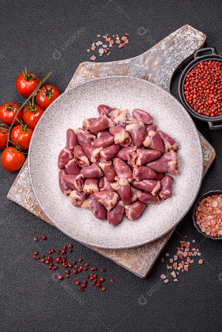 A imagem mostra corações de frango crus em uma tábua de madeira, acompanhados de pimenta rosa e tomates-cereja.