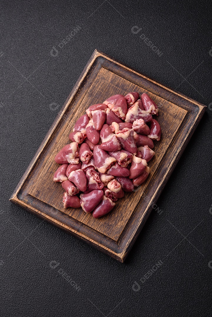A imagem mostra corações de frango crus em uma tábua de madeira, acompanhados de pimenta rosa e tomates-cereja.