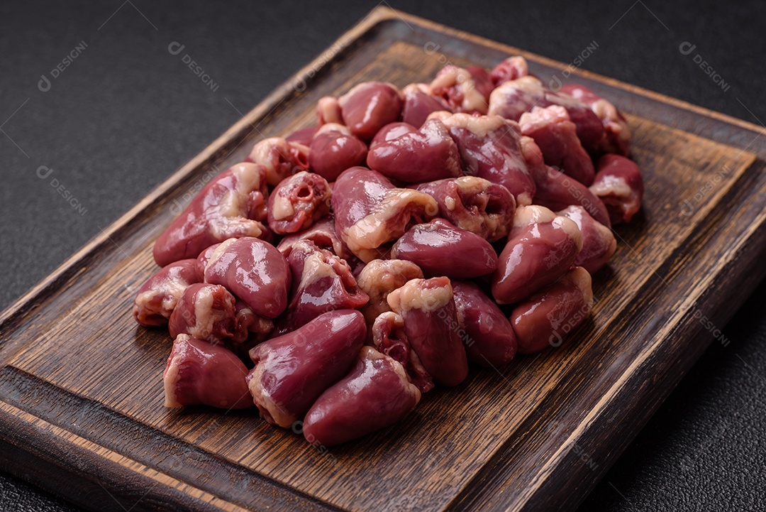 A imagem mostra corações de frango crus em uma tábua de madeira, acompanhados de pimenta rosa e tomates-cereja.