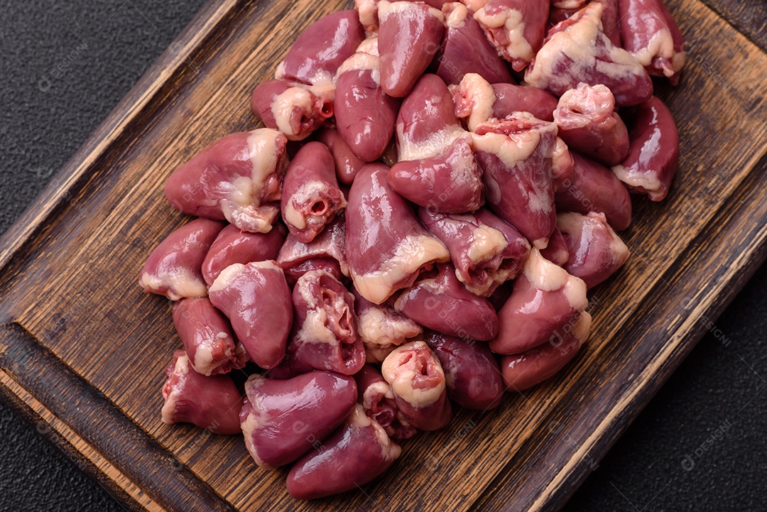 A imagem mostra corações de frango crus em uma tábua de madeira, acompanhados de pimenta rosa e tomates-cereja.