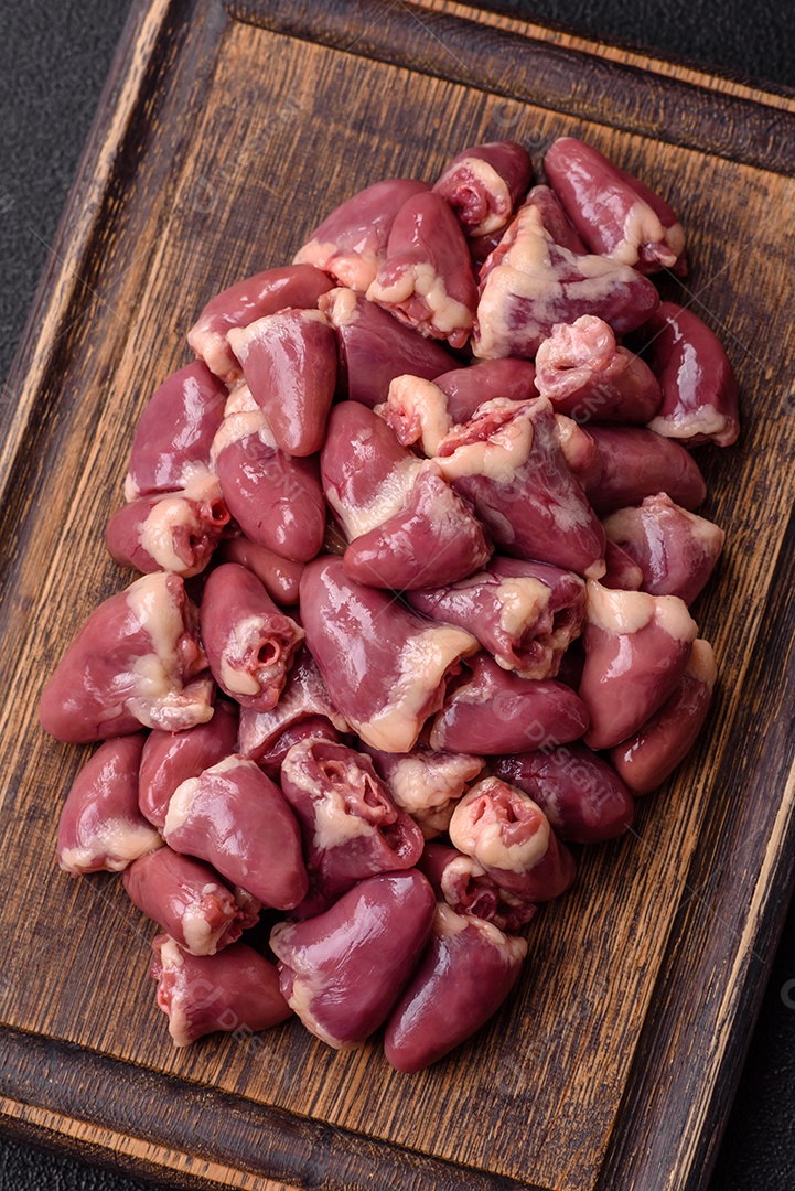 A imagem mostra corações de frango crus em uma tábua de madeira, acompanhados de pimenta rosa e tomates-cereja.