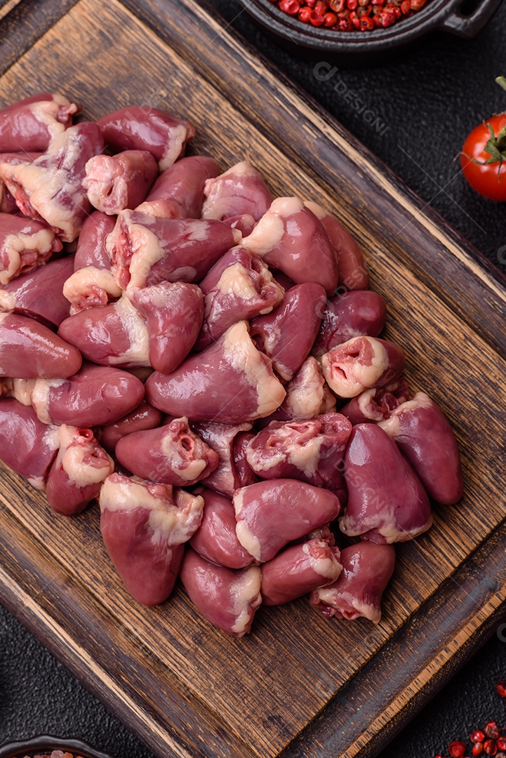 A imagem mostra corações de frango crus em uma tábua de madeira, acompanhados de pimenta rosa e tomates-cereja.