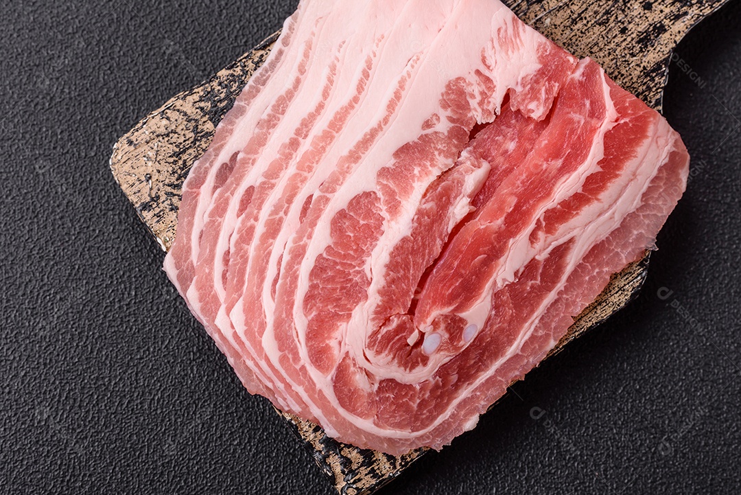 A imagem mostra fatias de barriga de porco crua, também conhecida como toucinho ou, em alguns casos, bacon. A barriga de porco