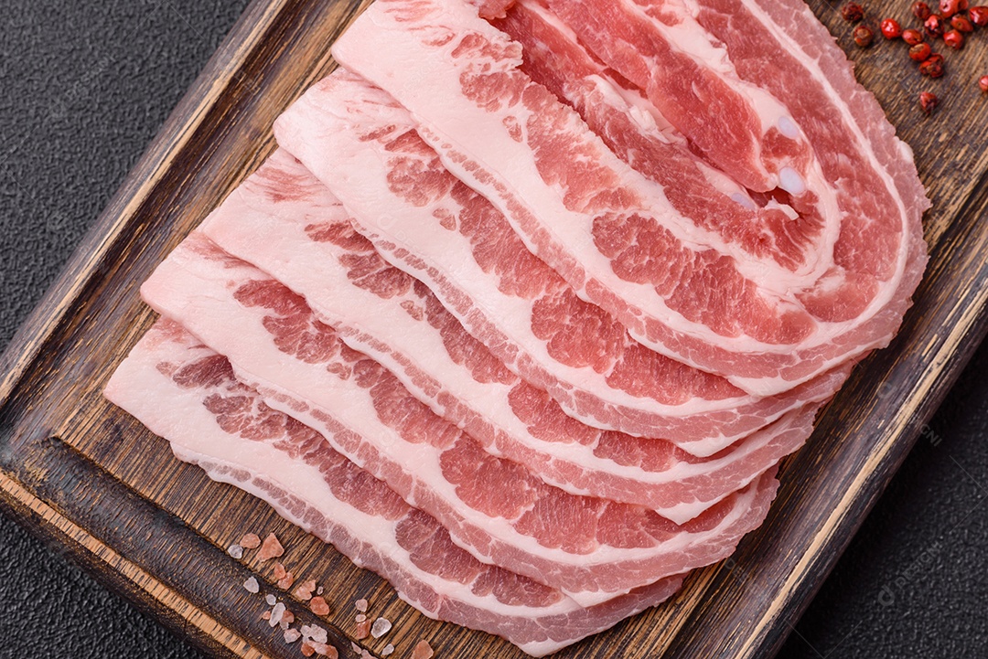 A imagem mostra fatias de barriga de porco crua, também conhecida como toucinho ou, em alguns casos, bacon. A barriga de porco