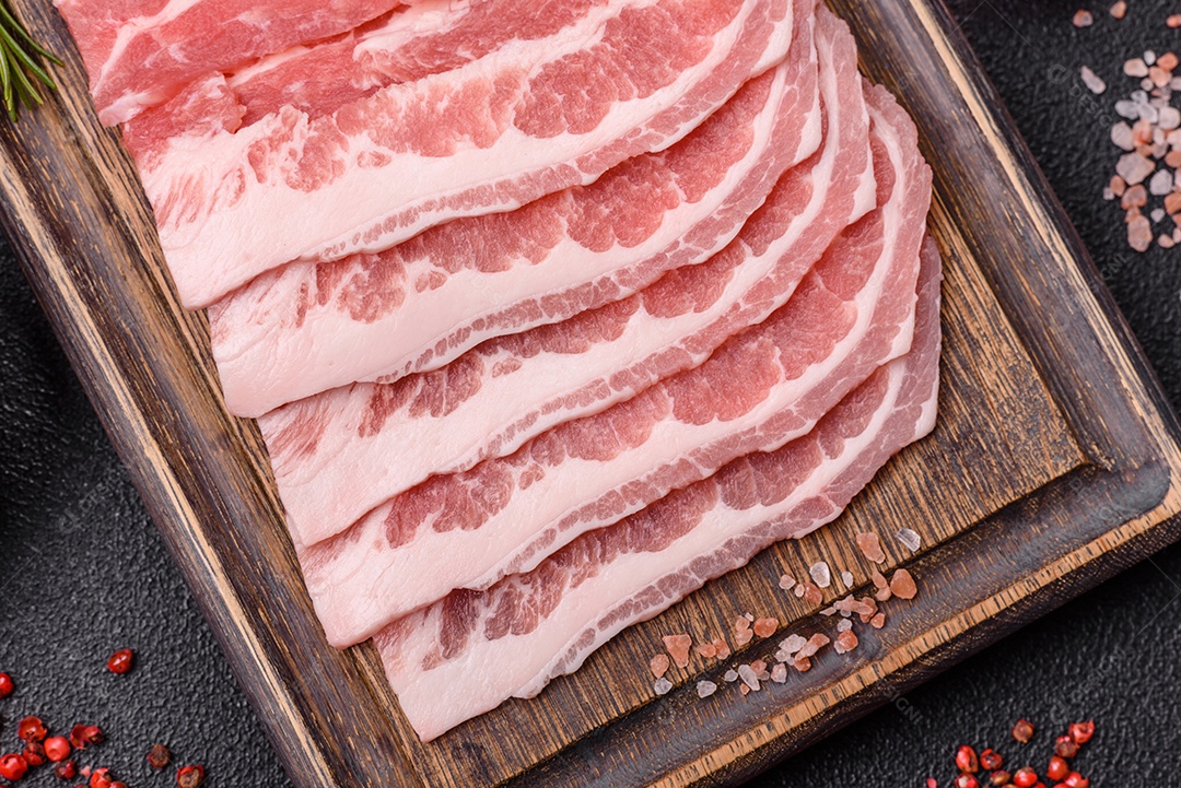 A imagem mostra fatias de barriga de porco crua, também conhecida como toucinho ou, em alguns casos, bacon. A barriga de porco