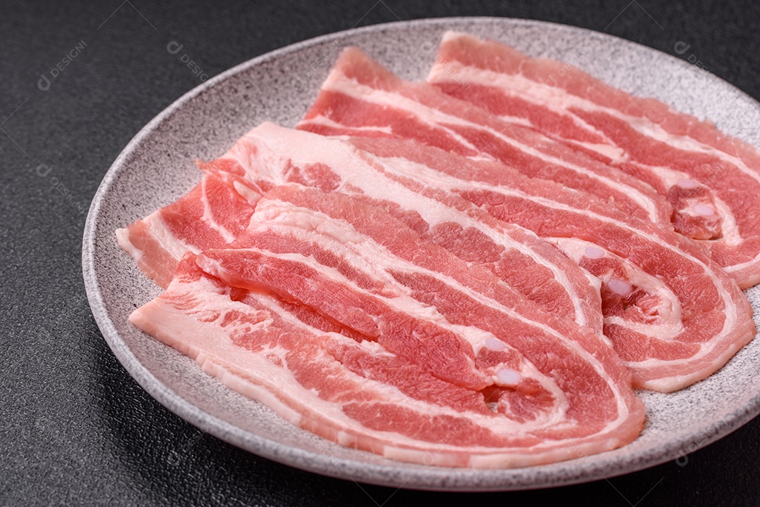 A imagem mostra fatias de barriga de porco crua, também conhecida como toucinho ou, em alguns casos, bacon. A barriga de porco