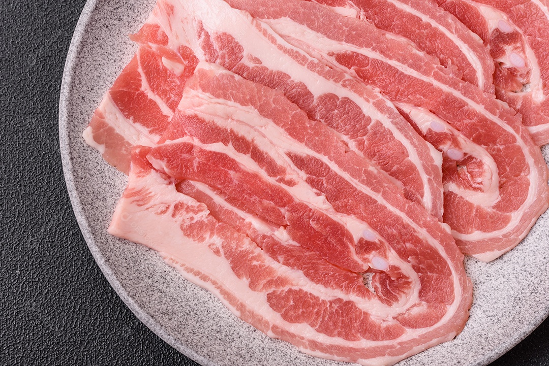 A imagem mostra fatias de barriga de porco crua, também conhecida como toucinho ou, em alguns casos, bacon. A barriga de porco