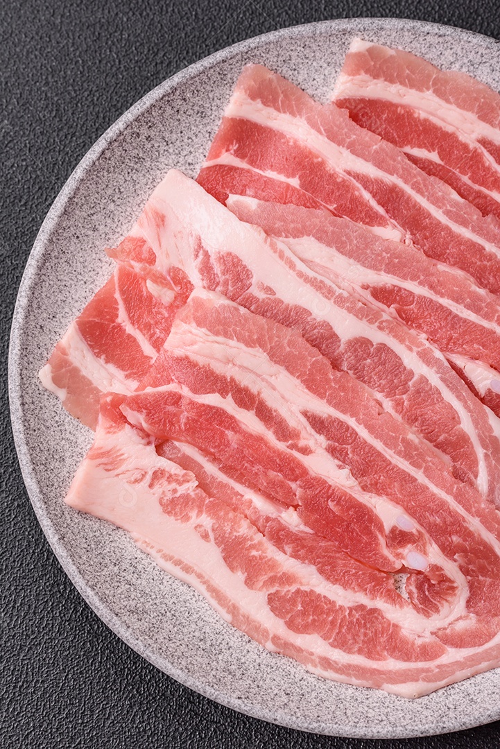 A imagem mostra fatias de barriga de porco crua, também conhecida como toucinho ou, em alguns casos, bacon. A barriga de porco