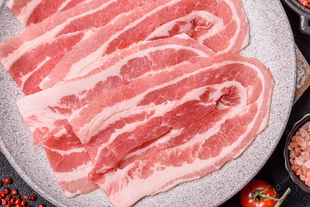 A imagem mostra fatias de barriga de porco crua, também conhecida como toucinho ou, em alguns casos, bacon. A barriga de porco