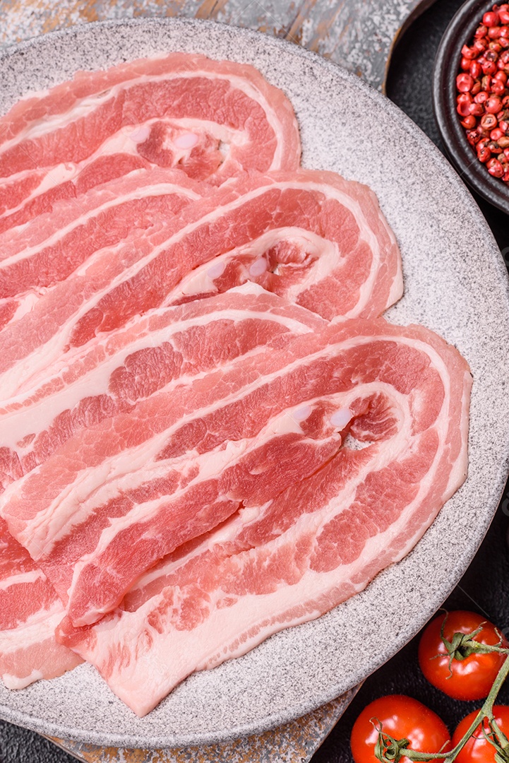 A imagem mostra fatias de barriga de porco crua, também conhecida como toucinho ou, em alguns casos, bacon. A barriga de porco