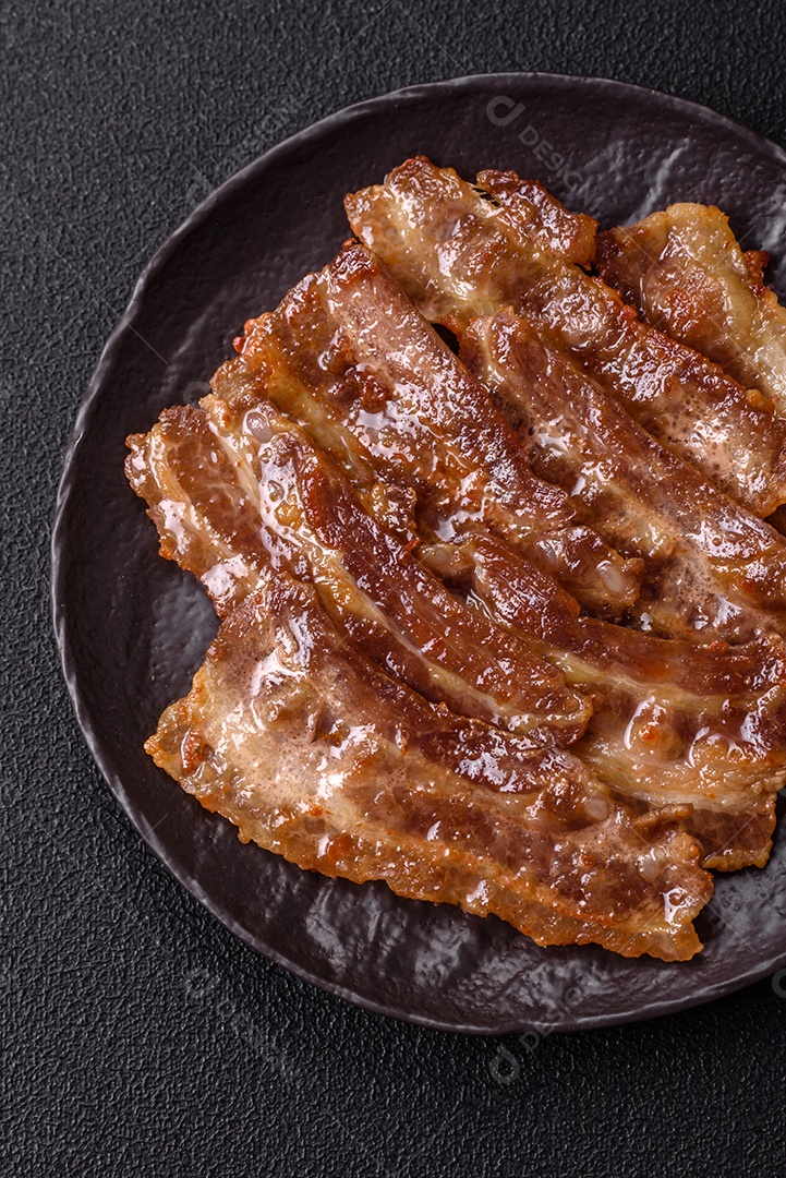 A imagem mostra toucinho frito em um prato, acompanhado de tomates-cereja e pimenta-rosa