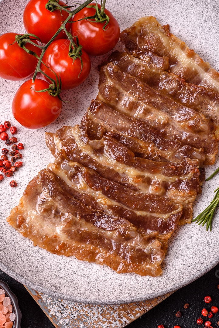 A imagem mostra toucinho frito em um prato, acompanhado de tomates-cereja e pimenta-rosa