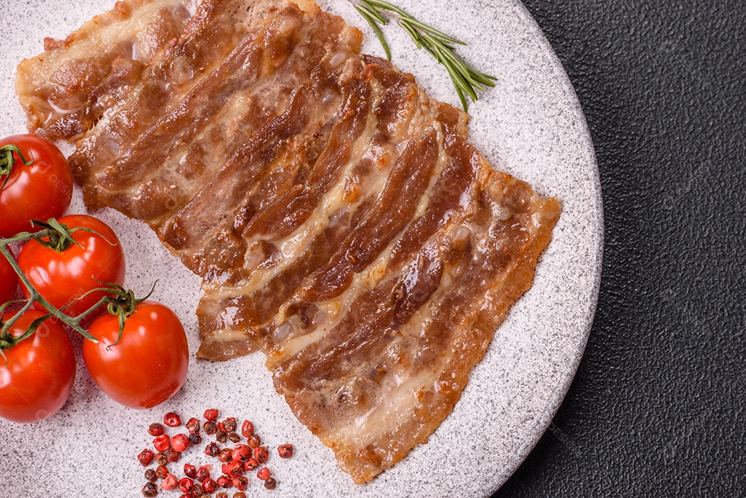 A imagem mostra toucinho frito em um prato, acompanhado de tomates-cereja e pimenta-rosa