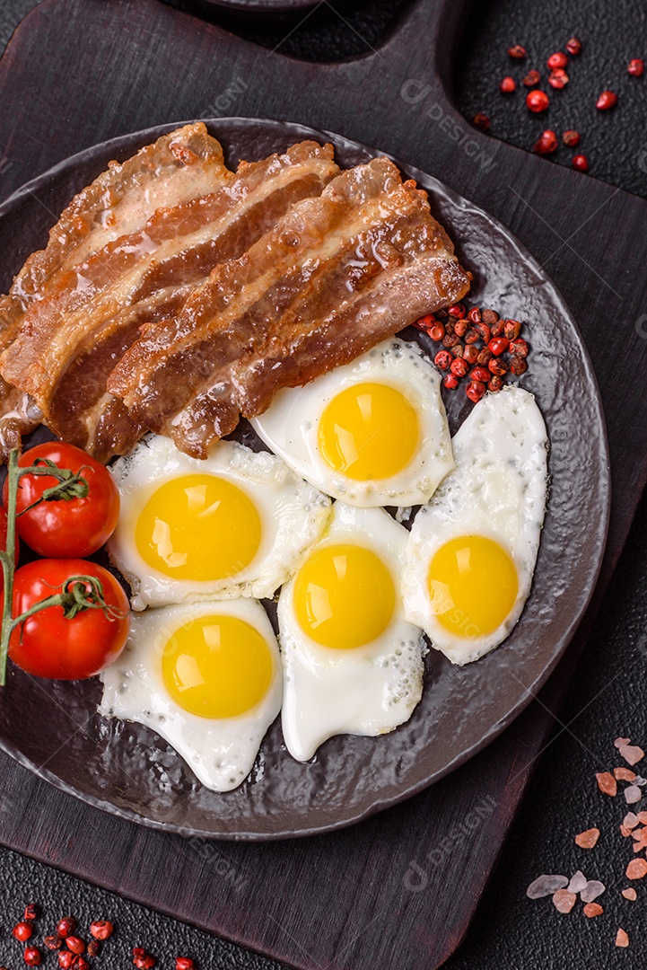 A imagem mostra um café da manhã farto com ovos fritos, bacon e tomates