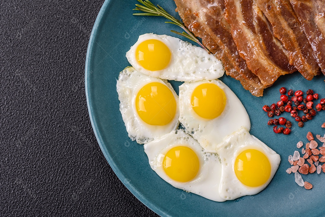A imagem mostra um café da manhã farto com ovos fritos, bacon e tomates