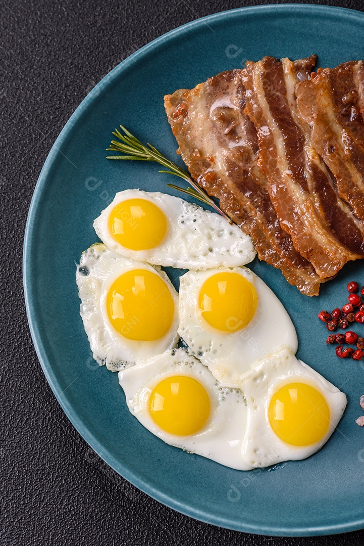 A imagem mostra um café da manhã farto com ovos fritos, bacon e tomates