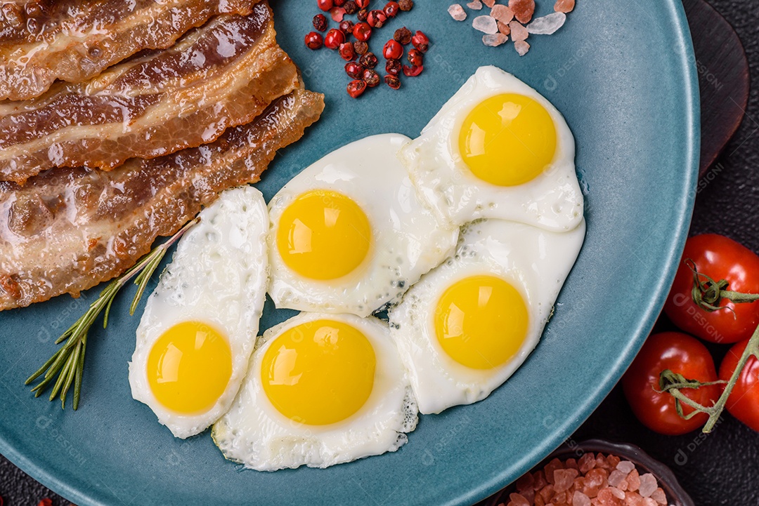 A imagem mostra um café da manhã farto com ovos fritos, bacon e tomates