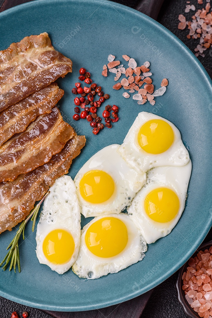 A imagem mostra um café da manhã farto com ovos fritos, bacon e tomates