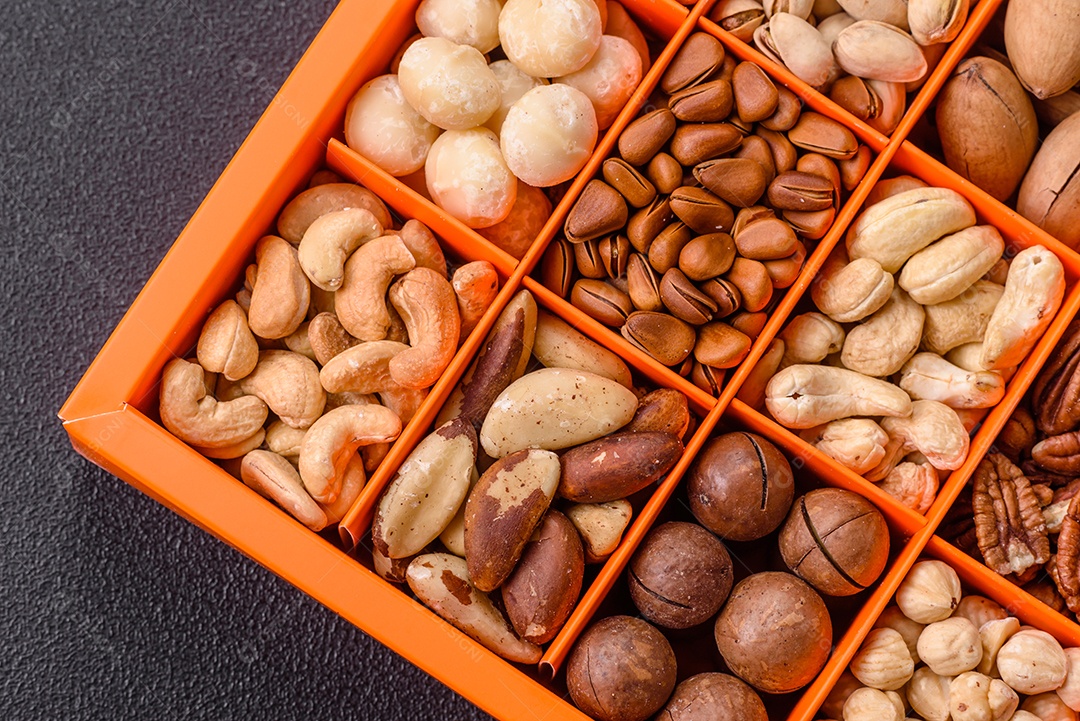Imagem mostra uma variedade de oleaginosas, comumente chamadas de castanhas e nozes, em uma caixa dividida em compartimentos.