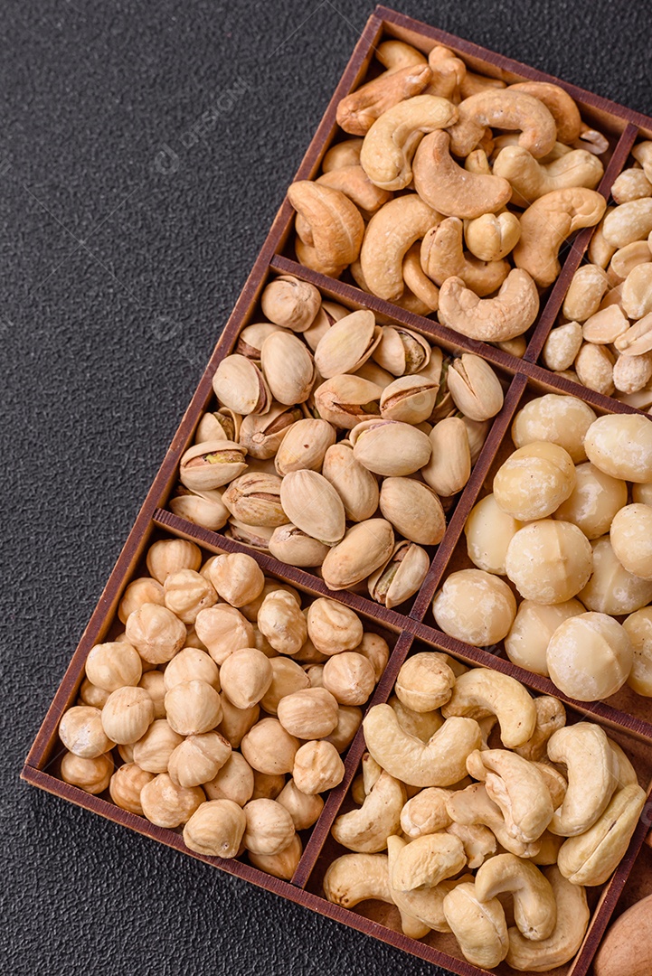 Imagem mostra uma variedade de oleaginosas, comumente chamadas de castanhas e nozes, em uma caixa dividida em compartimentos. Comida