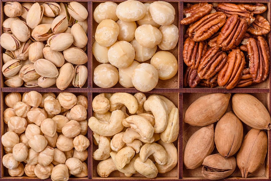 Imagem mostra uma variedade de oleaginosas, comumente chamadas de castanhas e nozes, em uma caixa dividida em compartimentos.
