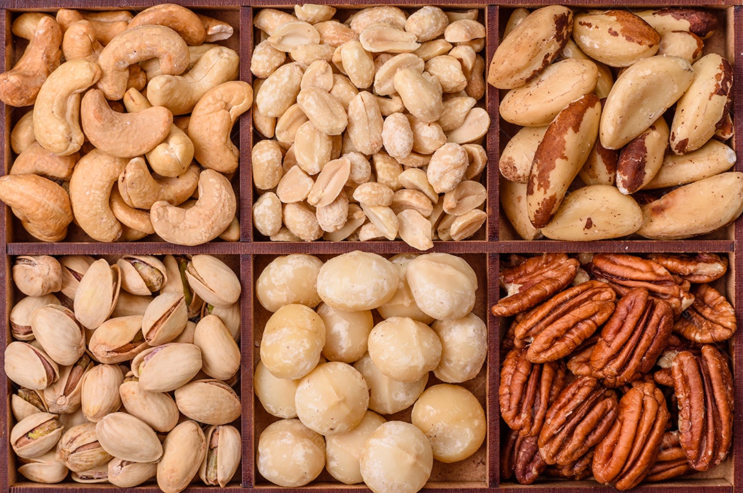 Imagem mostra uma variedade de oleaginosas, comumente chamadas de castanhas e nozes, em uma caixa dividida em compartimentos.