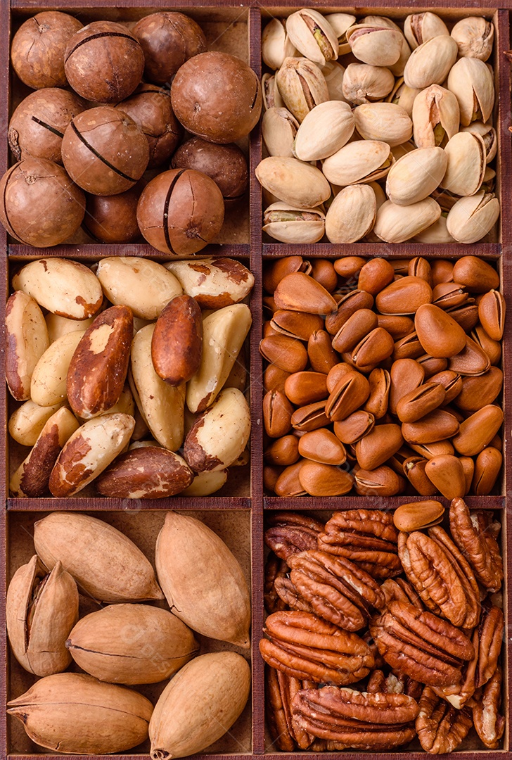 Imagem mostra uma variedade de oleaginosas, comumente chamadas de castanhas e nozes, em uma caixa dividida em compartimentos.