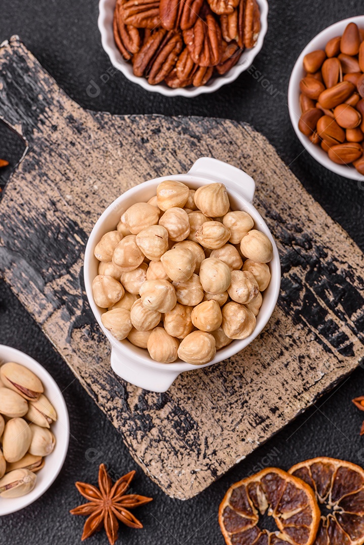 A imagem mostra uma variedade de nozes e frutas secas dispostas sobre uma tábua de madeira e um fundo escuro.
