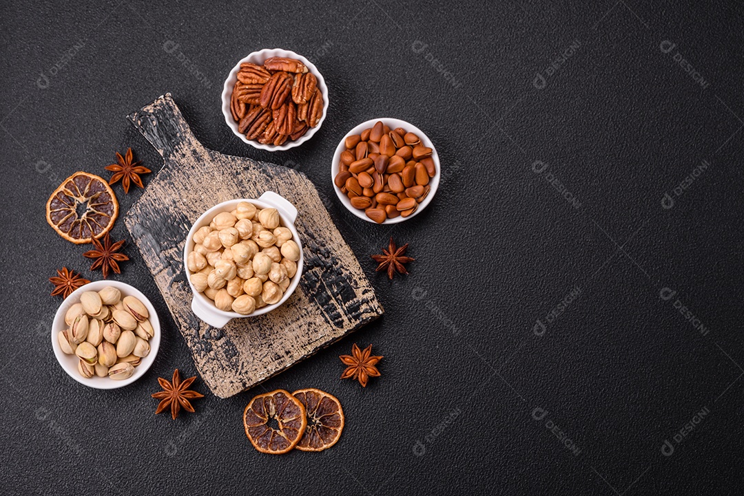 A imagem mostra uma variedade de nozes e frutas secas dispostas sobre uma tábua de madeira e um fundo escuro.