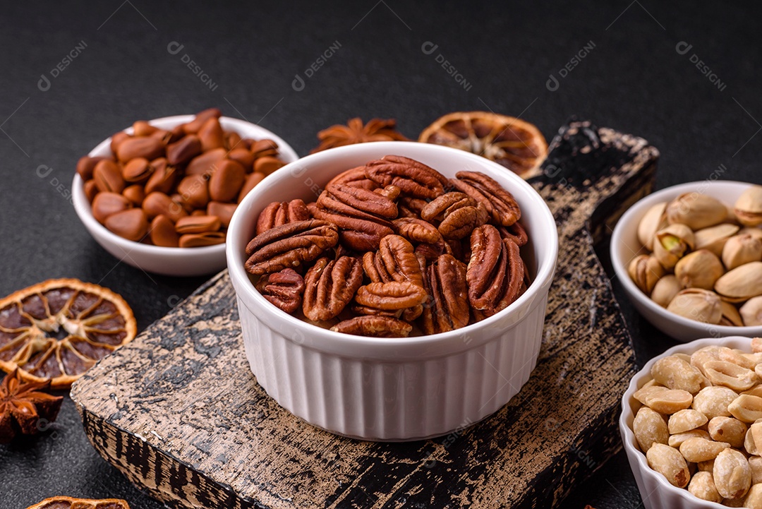 A imagem mostra uma variedade de nozes e frutas secas dispostas sobre uma tábua de madeira e um fundo escuro.